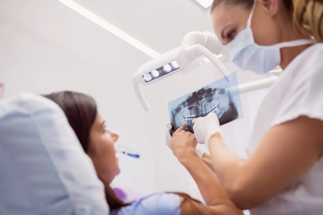 La dentista enseña una radiografía panorámica a la paciente, tumbada en el sillón