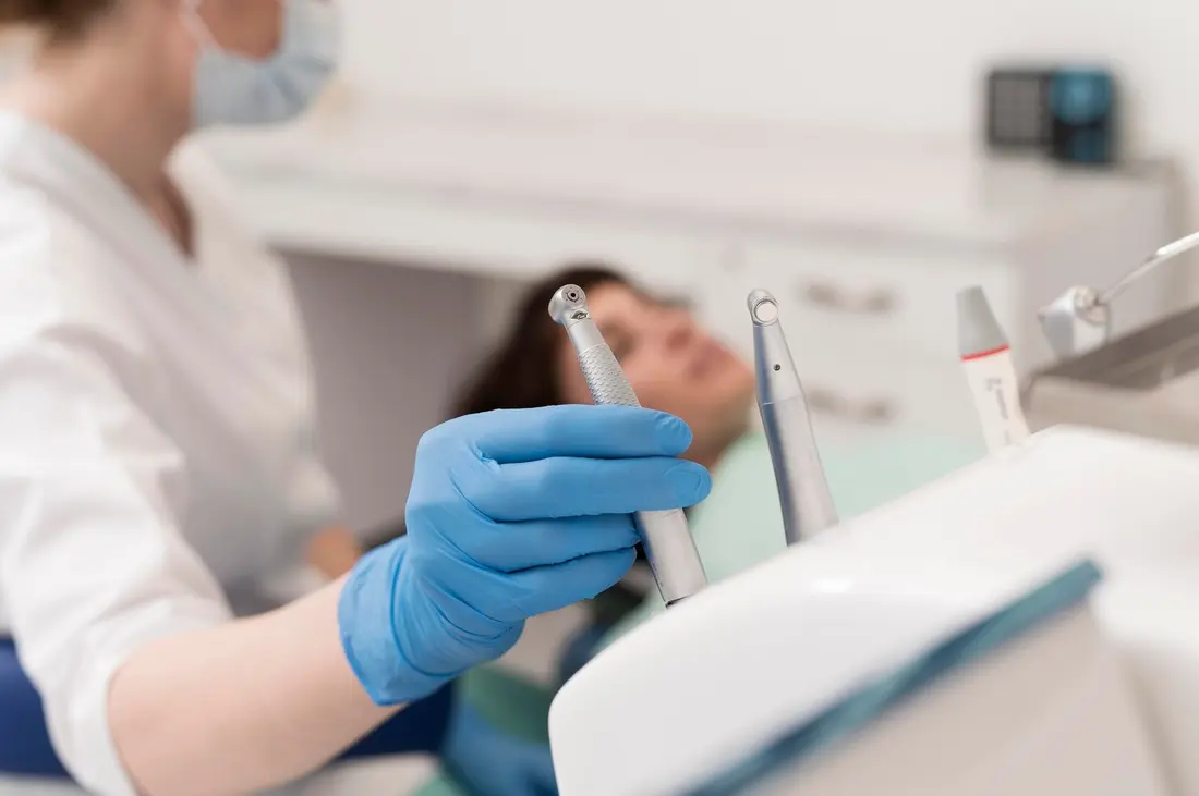 Una dentista con guantes sostiene el instrumental junto a la paciente en el sillón